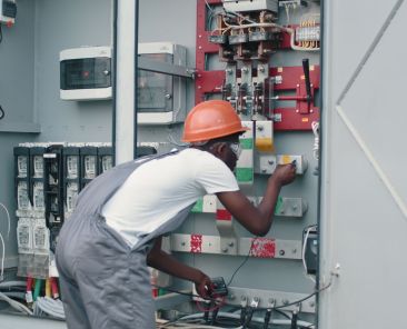 african-american-man-in-overalls-safety-helmet-and-glasses-working-on-switchgear-at-so-SBI-351269919